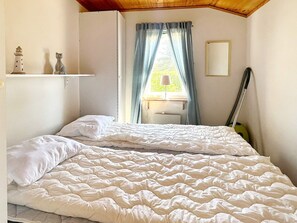 A bedroom with a bed, a window with curtains, a lamp, and a wall-mounted shelf with decorative items. - 5 Person Holiday Home in Skummeslovsstrand (Skummesloevsstrand)