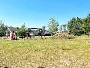 Een grasveld met een schommel, een kleine speelconstructie en een zandheuvel.