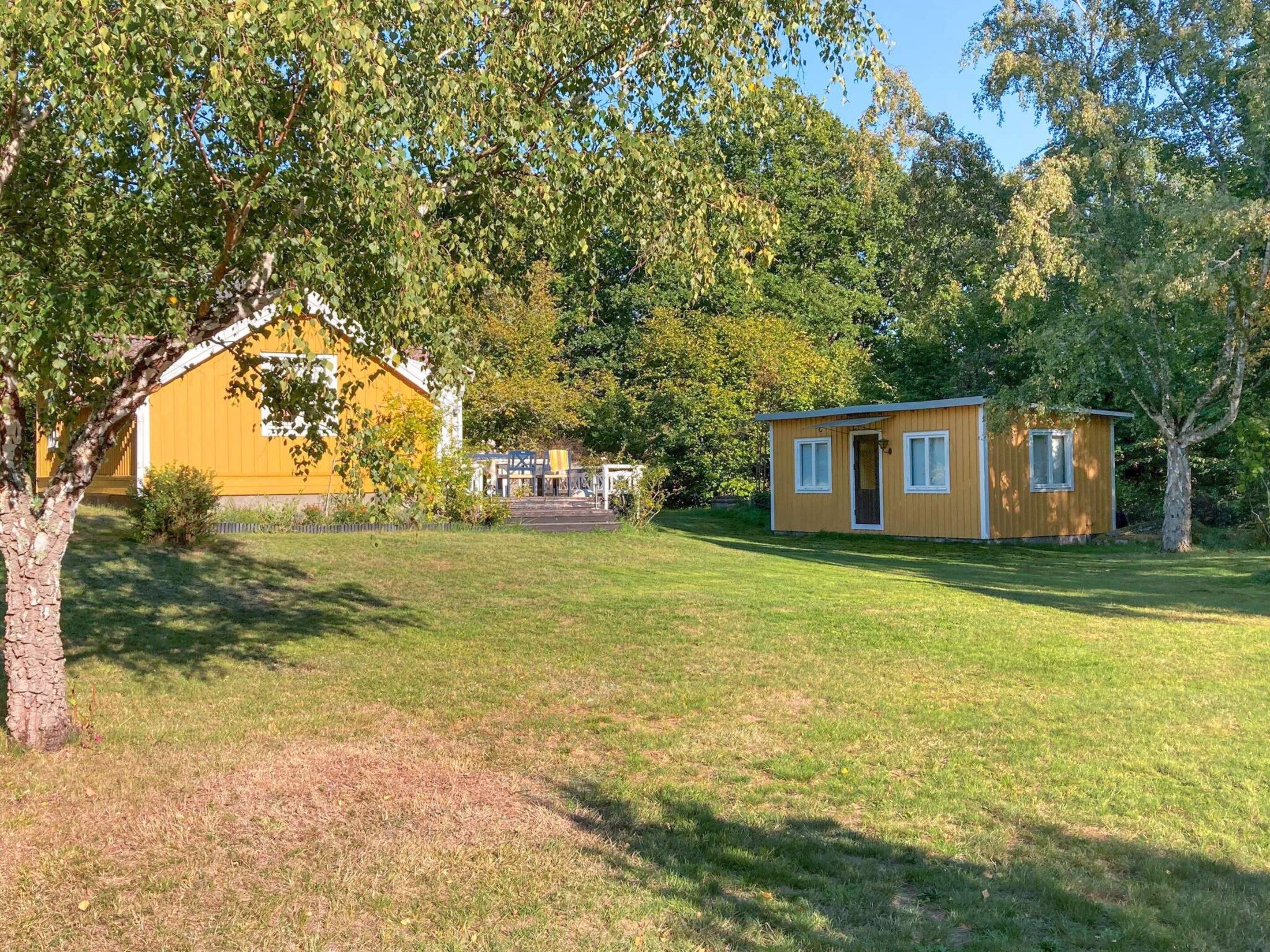 A yellow building with a small attached structure, surrounded by trees and grass.