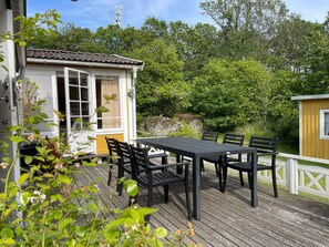 A wooden deck with a table and chairs, a small building with a window, and a white fence.