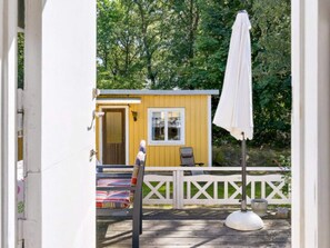 A wooden deck with a white umbrella, a yellow building with a door, and a white fence. - 6 Person Holiday Home in Ramdala (Ramdala)