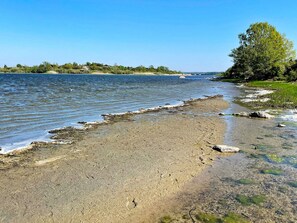 A riverbank with clear water, a sandy shore, and a tree on the right. - 6 Person Holiday Home in Ramdala (Ramdala)