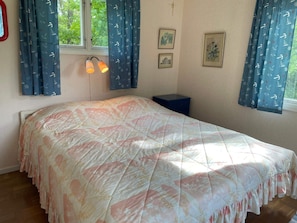 A bedroom with a bed, a window with curtains, a bedside table, and wall-mounted lights.
