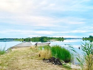 A calm lake with a wooden dock extending into the water, surrounded by grassy banks and some vegetation. - 6 Person Holiday Home in Ramdala (Ramdala)