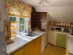 A kitchen with a sink, a microwave, and a window with floral curtains. - 6 Person Holiday Home in Ramdala (Ramdala)