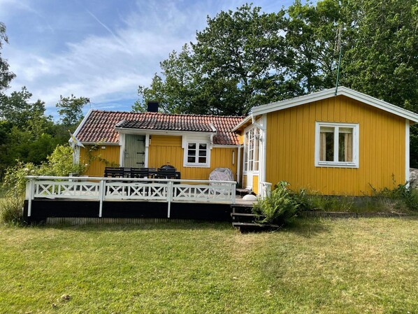 A yellow house with a red-tiled roof, a wooden deck, and a small dock extending into a body of water.