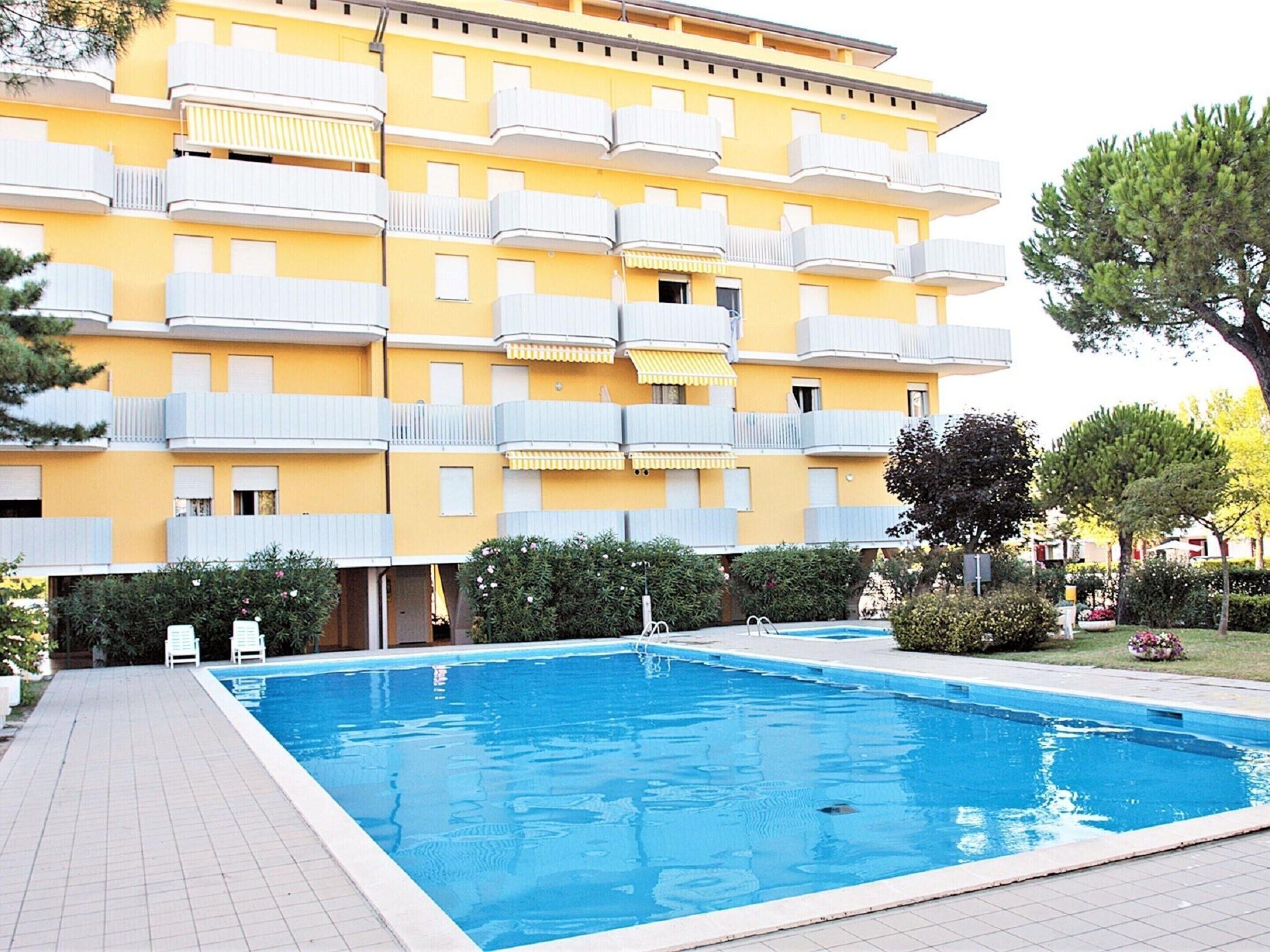 Un edificio amarillo de varios pisos con balcones, piscina y jardín.