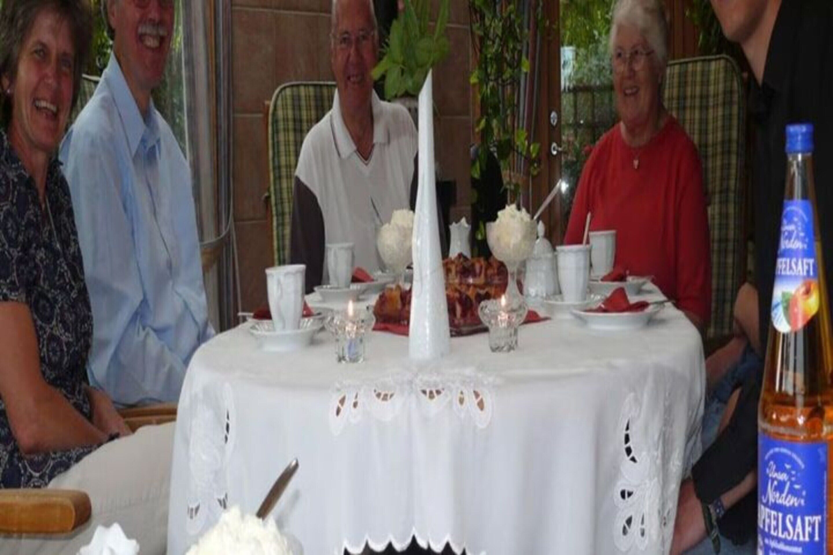 A dining table set with white tablecloths, candles, and a bottle of beer.
