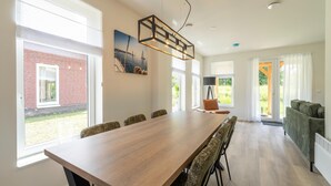 A modern dining area with a long wooden table, chairs, and a pendant light. - Holiday Home by Lake Beach Simonshaven (Simonshaven)