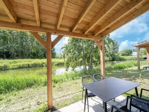 A wooden pavilion with a table and chairs, overlooking a river and greenery. - Holiday Home by Lake Beach Simonshaven (Simonshaven)