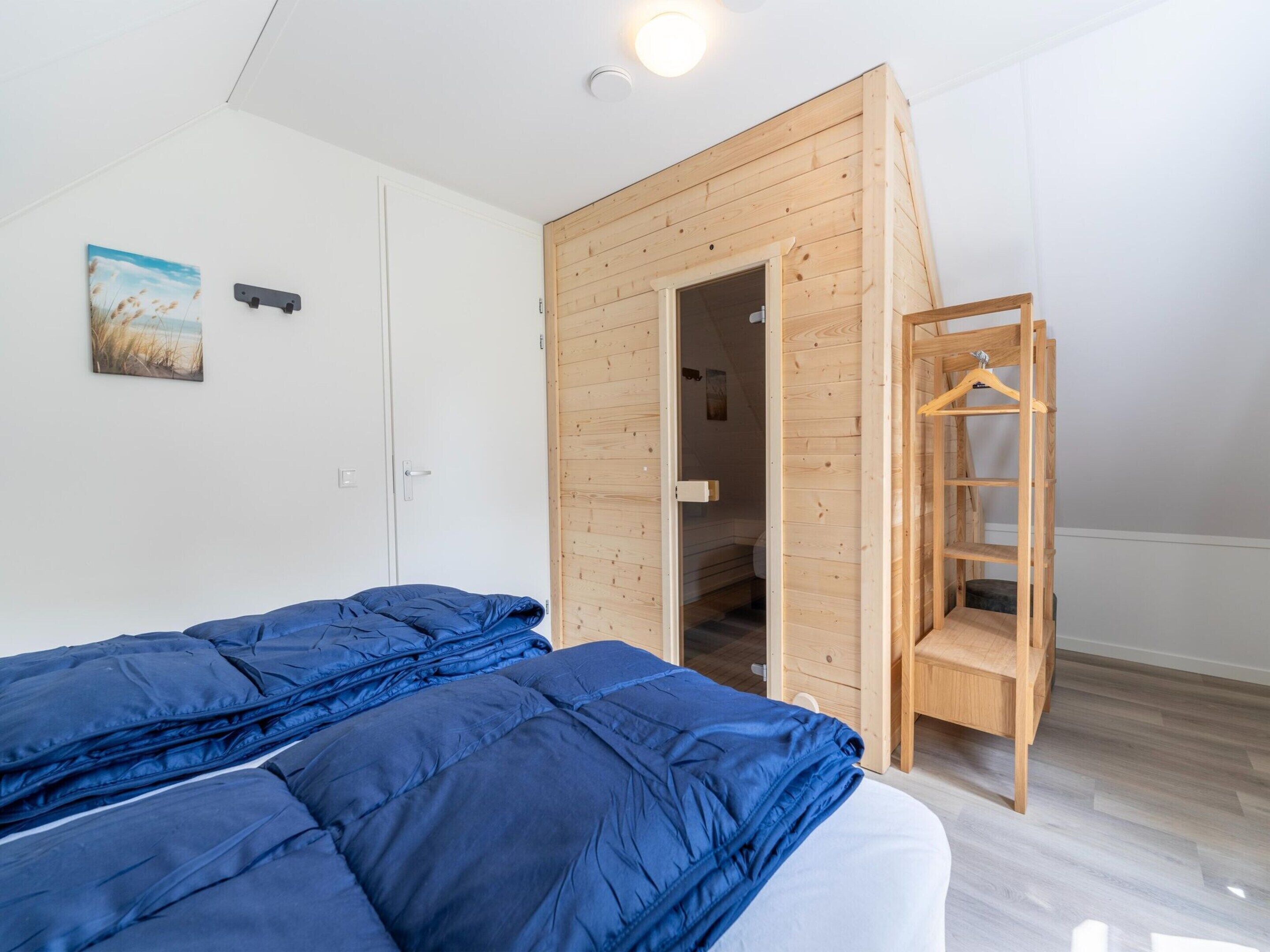 A bedroom with two beds, a wooden wardrobe, a wooden ladder, and a door leading to a bathroom.