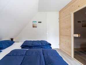 A bedroom with a sloped ceiling, a white wardrobe, a wooden door, and a bed with blue bedding. - Holiday Home by Lake Beach Simonshaven (Simonshaven)