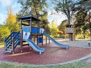 A playground with a slide and climbing structures, surrounded by trees and a paved area. - 2 Person Holiday Home in Norrkoping (Norrköping)