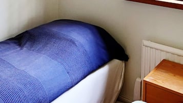 A single bed with a blue mattress and white bedding, a wooden nightstand, and a white radiator.