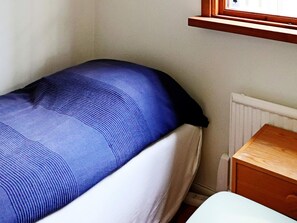 Een enkel bed met een blauwe matras en witte beddengoed, een houten nachtkastje en een witte radiator.