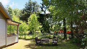 Un espace extérieur clos, avec une table et des bancs en bois, un bâtiment doté d’une fenêtre et des arbres.