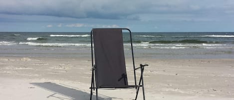 A beach chair on a sandy beach with waves in the background.