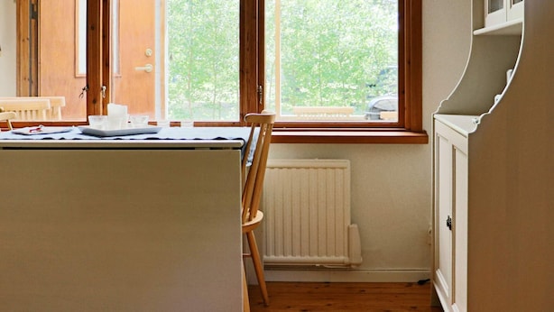Una cocina con una mesa de madera, sillas, un ventanal y un radiador.