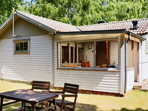 A single-story house with a covered porch, a window with a view of the interior, and a small table with chairs outside. - 5 Person Holiday Home in Skummeslovsstrand (Skummesloevsstrand)