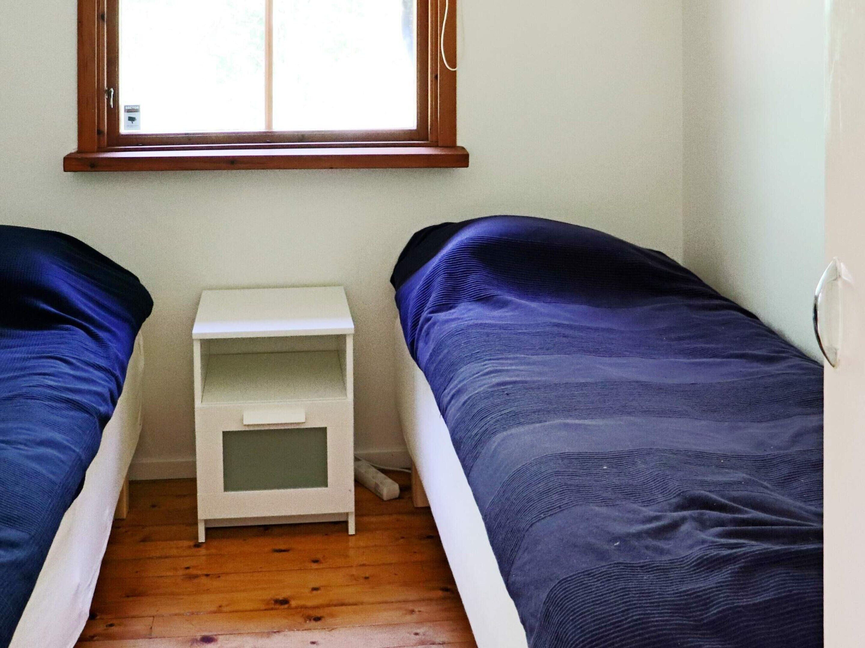 A small room with two single beds, a white nightstand, and a window.