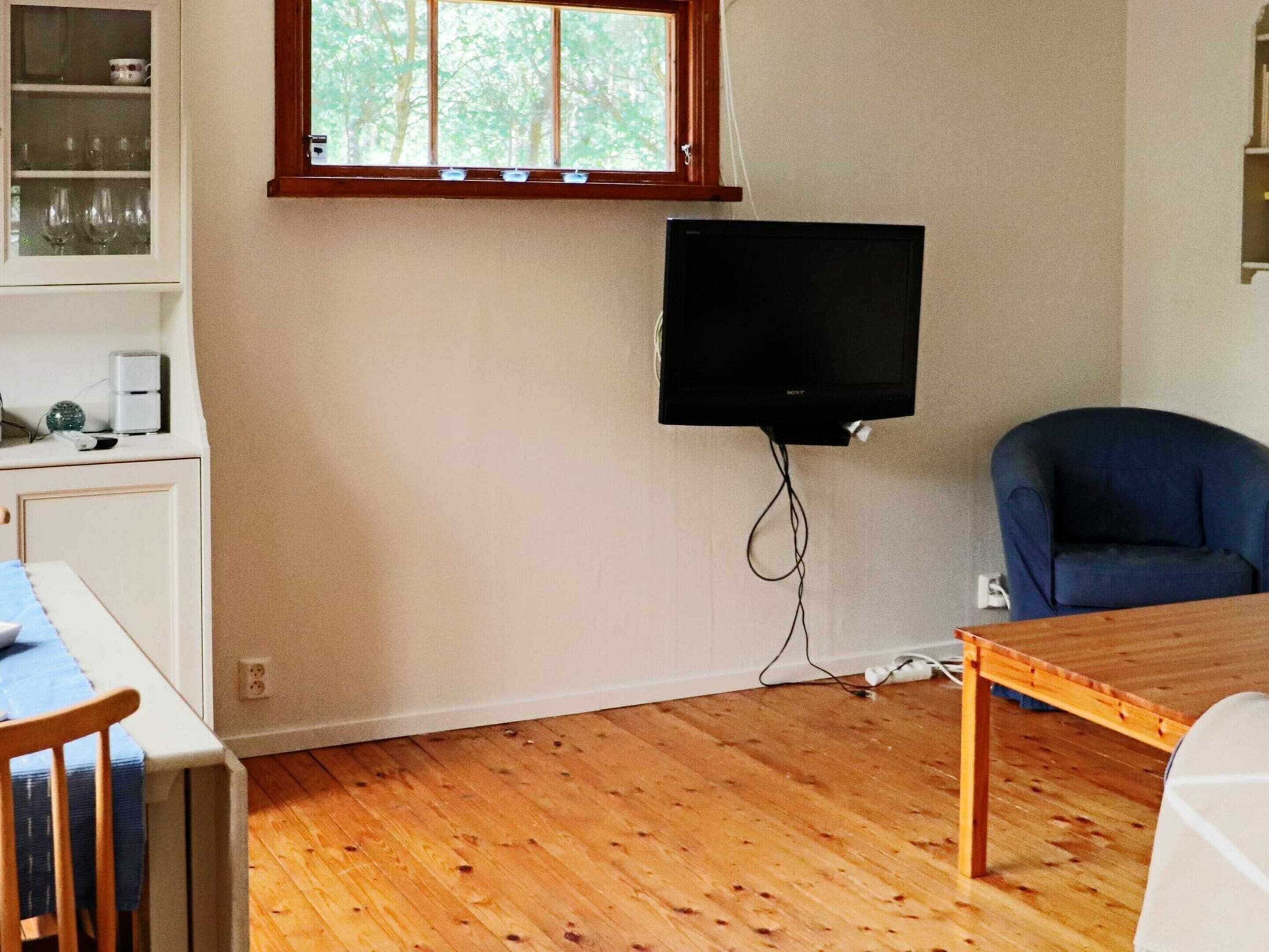 Een kamer met houten vloer, een aan de muur bevestigde televisie, een blauwe stoel en een tafel.