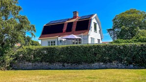 Punakattoisessa, kahden kerroksen talossa on suuret ikkunat ja edessä kivimuuri.