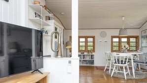 A living room with a flat-screen TV, wooden entertainment unit, and a dining area with a table and chairs.