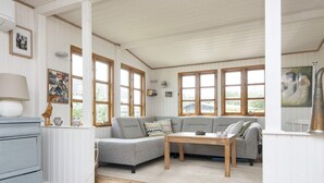 A cozy living room with a grey sectional sofa, a wooden coffee table, and a large window with wooden frames.