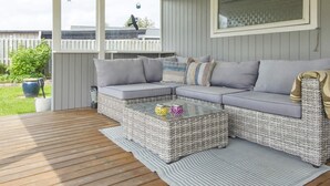 A covered patio area with a grey woven sofa set, a glass coffee table, and a striped rug.