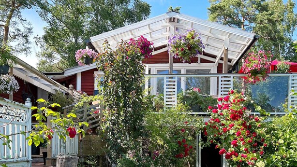 A house with a white exterior, a red roof, and a garden with various plants and flowers. - 4 Person Holiday Home in Arsta Havsbad (Haninge)