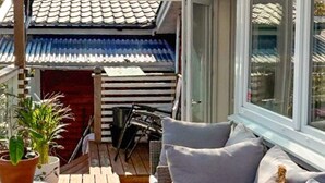 A wooden deck with a sofa and chairs, potted plants, and a view of a building with a tiled roof. - 4 Person Holiday Home in Arsta Havsbad (Haninge)