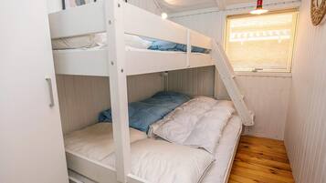 Une chambre avec un lit superposé, un plancher en bois, une fenêtre avec des stores et un luminaire suspendu.