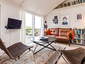 A living room with a brown leather sofa, two wicker chairs, a coffee table, a television, and a bookshelf filled with books. - 4 Star Holiday Home in Hjorring (Hjørring)