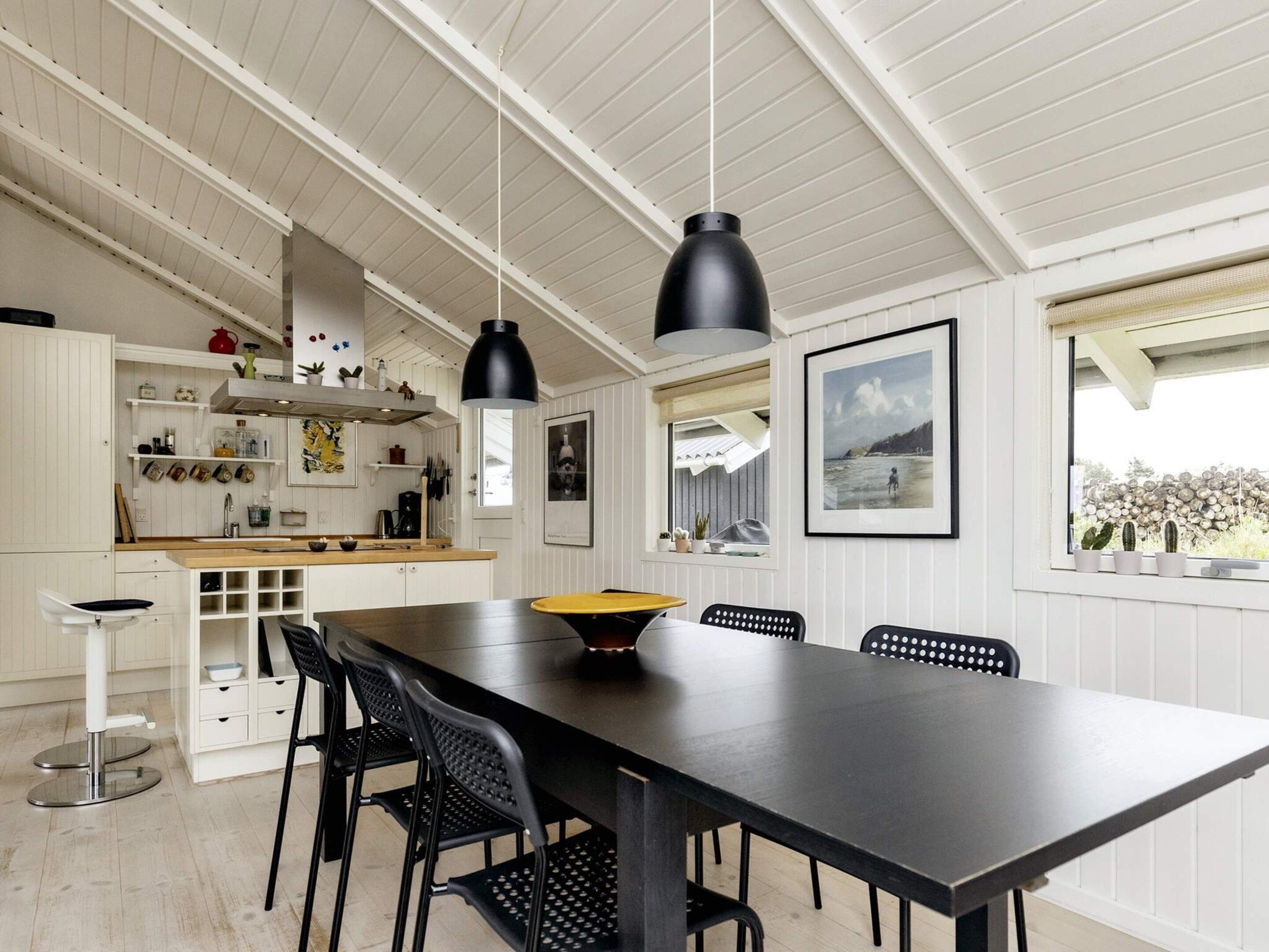 Una cocina moderna con armarios blancos, un comedor con mesa negra e iluminación colgante.