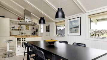 Una cocina moderna con armarios blancos, un comedor con mesa negra e iluminación colgante.