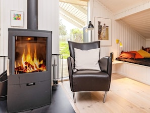 Une pièce chaleureuse avec un poêle à bois, un fauteuil en cuir, un lit agrémenté de coussins colorés et un tableau accroché au mur.