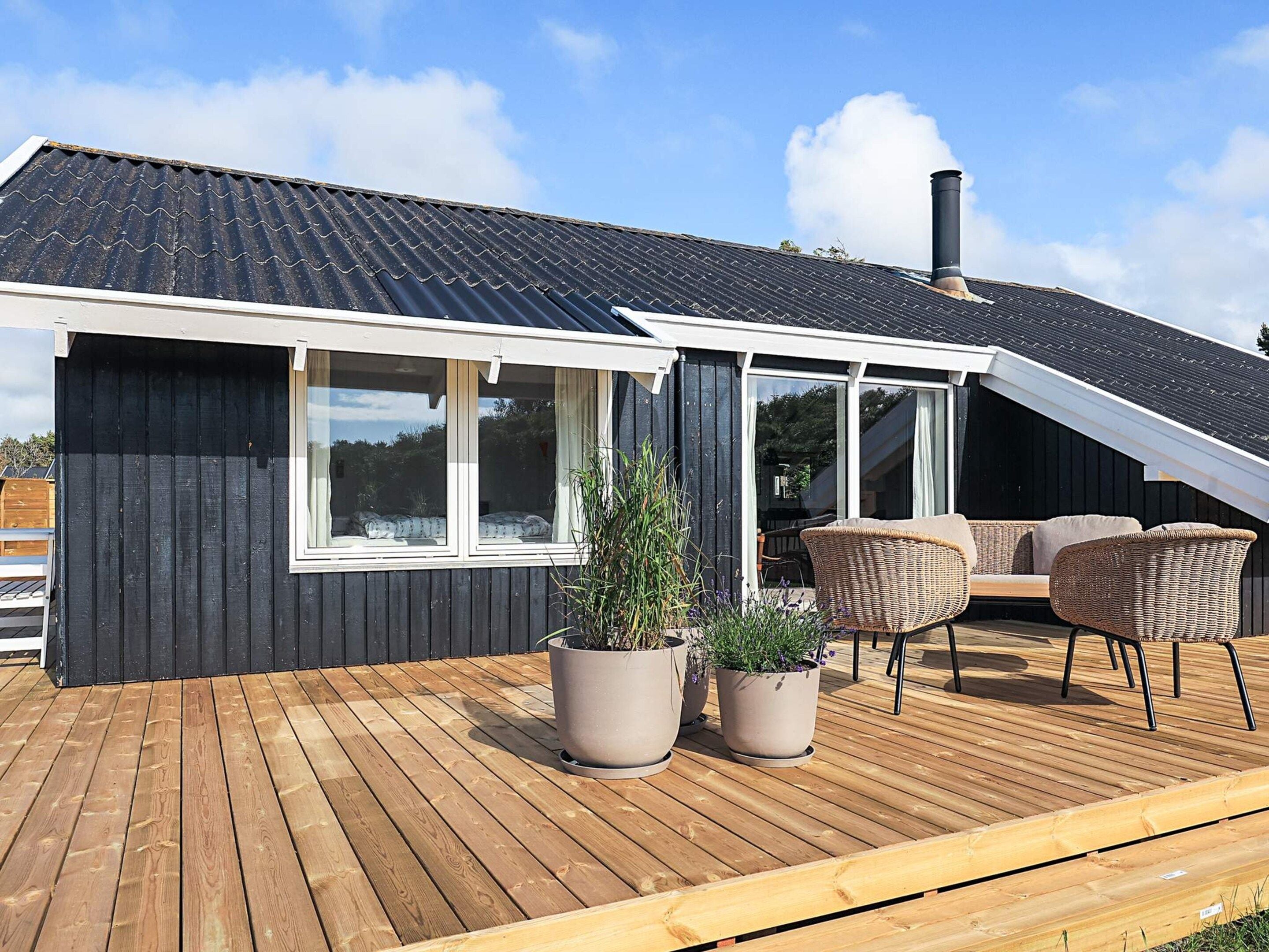 Une maison moderne dotée d’une terrasse en bois, de grandes fenêtres et de mobilier d’extérieur.
