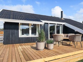Una casa moderna con terraza de madera, ventanas amplias y mobiliario exterior.