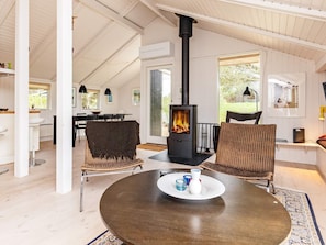 A cozy room with a round table, two wicker chairs, a black wood-burning stove, and a dining area with a table and chairs. - 4 Star Holiday Home in Hjorring (Hjørring)