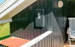 Un mur extérieur en bois foncé, avec une porte blanche et une petite fenêtre.