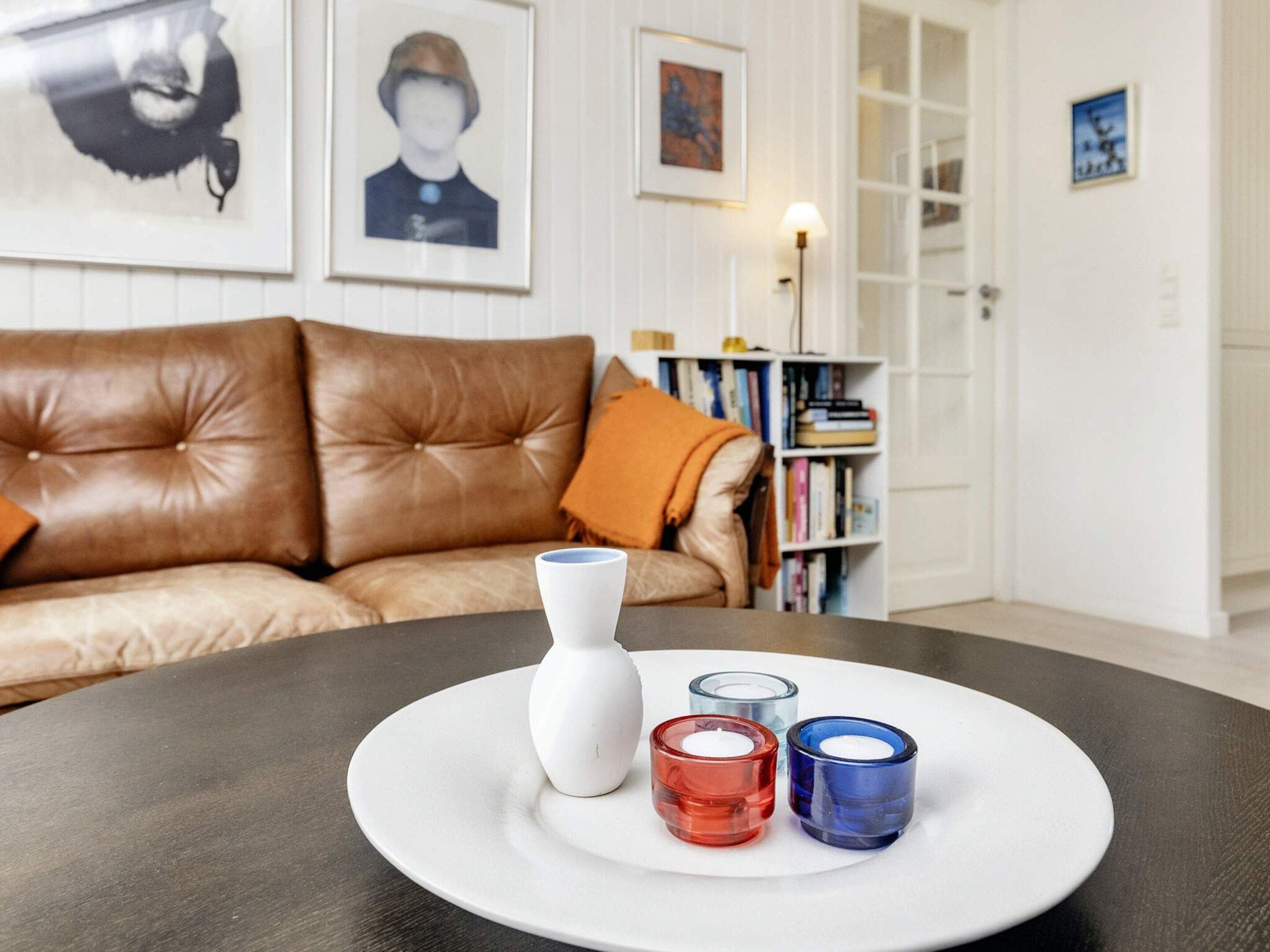 Una habitación con un sofá de cuero marrón, un jarrón blanco y tres candelabros sobre una mesa redonda.
