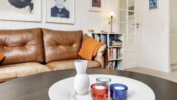 Una habitación con un sofá de cuero marrón, un jarrón blanco y tres candelabros sobre una mesa redonda.
