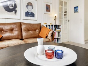 Ein Zimmer mit einem braunen Ledersofa, einer weißen Vase und drei Kerzenhaltern auf einem runden Tisch.