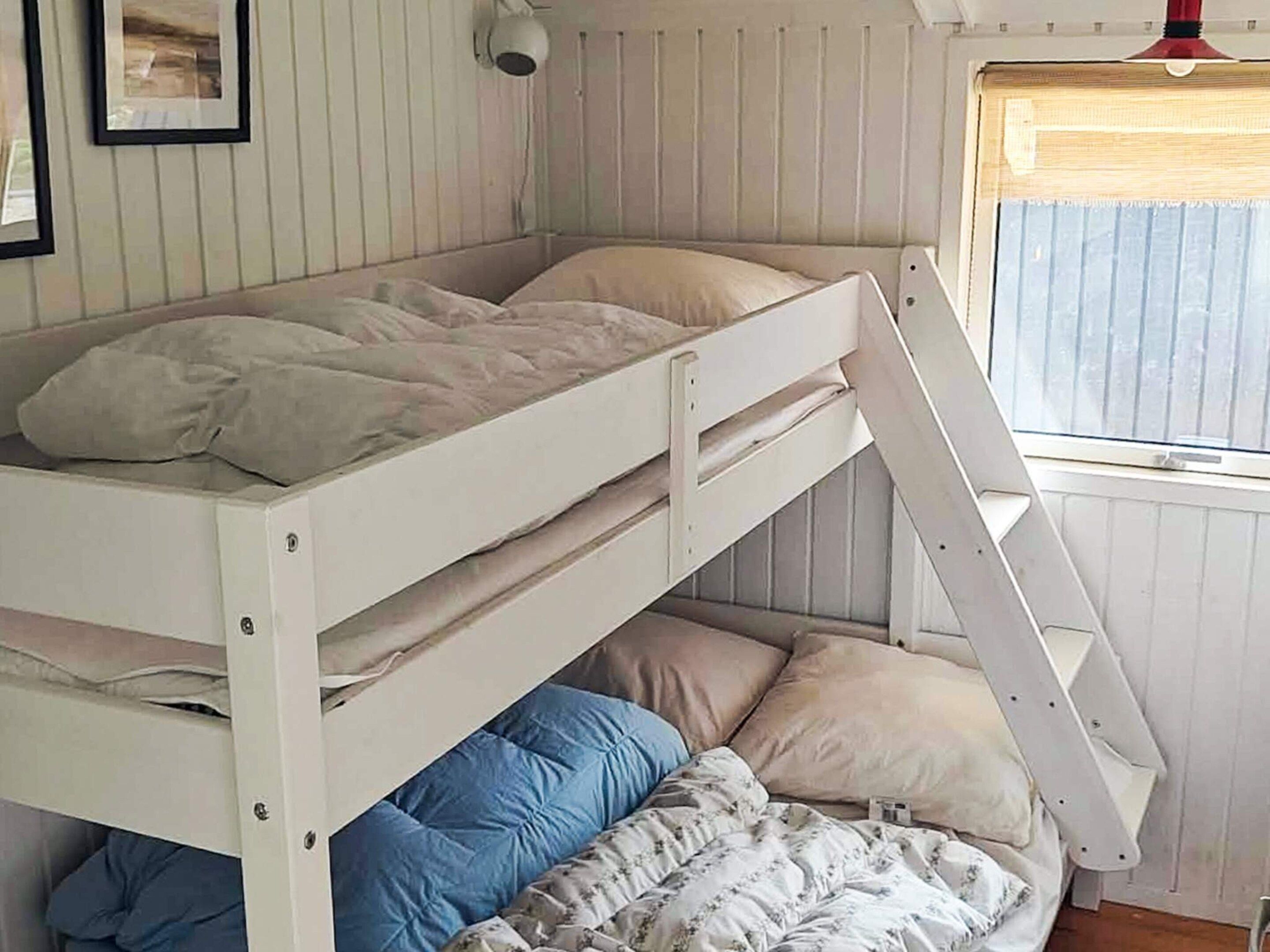 A bunk bed with a ladder, a window with blinds, and a wall-mounted light fixture.
