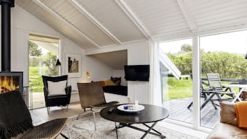 A cozy living room with a fireplace, comfortable seating, a flat-screen TV, and a large window offering a view of the outdoors.