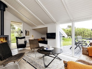 A cozy living room with a fireplace, comfortable seating, a flat-screen TV, and a large window offering a view of the outdoors. - 4 Star Holiday Home in Hjorring (Hjørring)