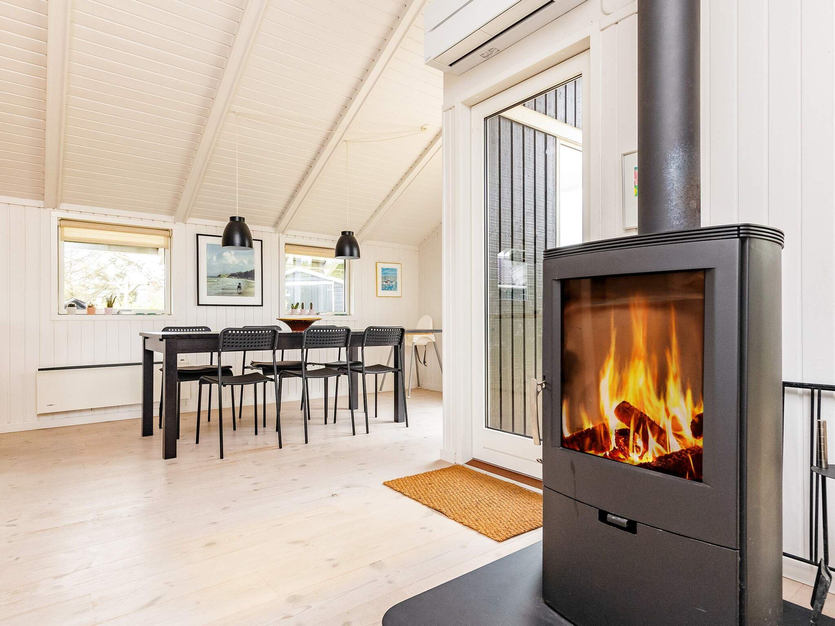 Et moderne køkken med en brændeovn, et spiseområde med stole og et stort vindue.