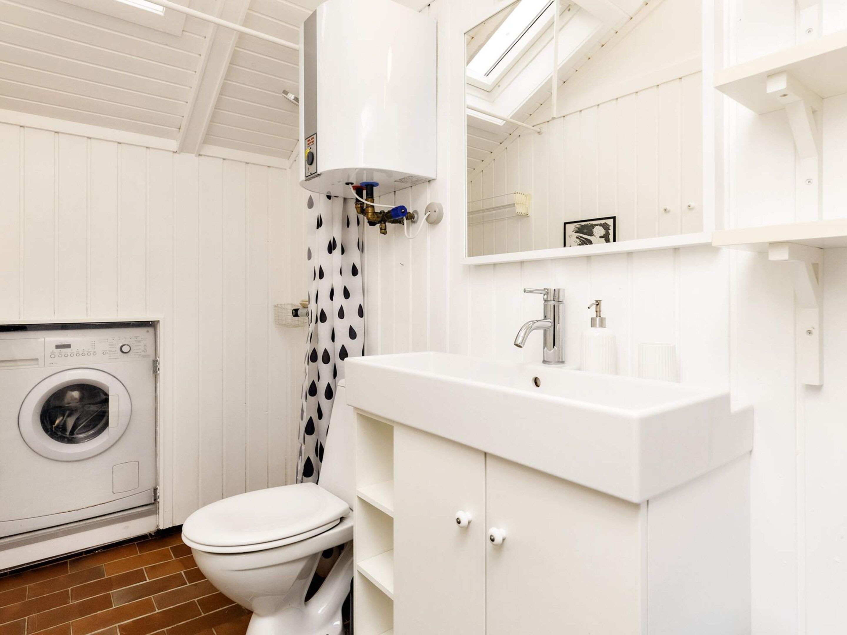 A bathroom with a washing machine, toilet, and a sink with a mirror above.