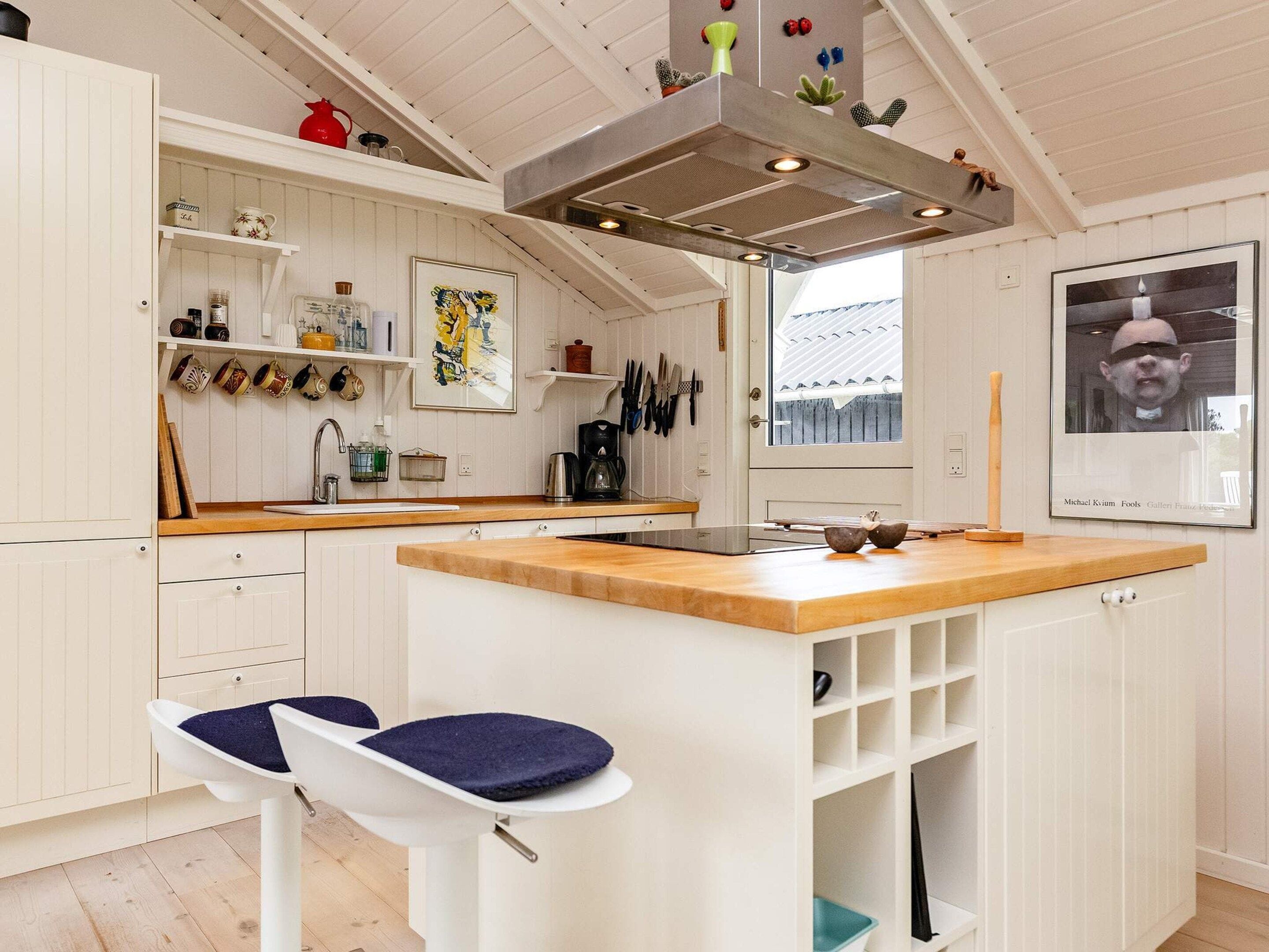 Una cocina con isla de madera, armarios blancos y una pata de gallo para colgar ollas.