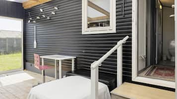 A room with a bed, a small table, a chair, a mirror, and a staircase leading to a bathroom.